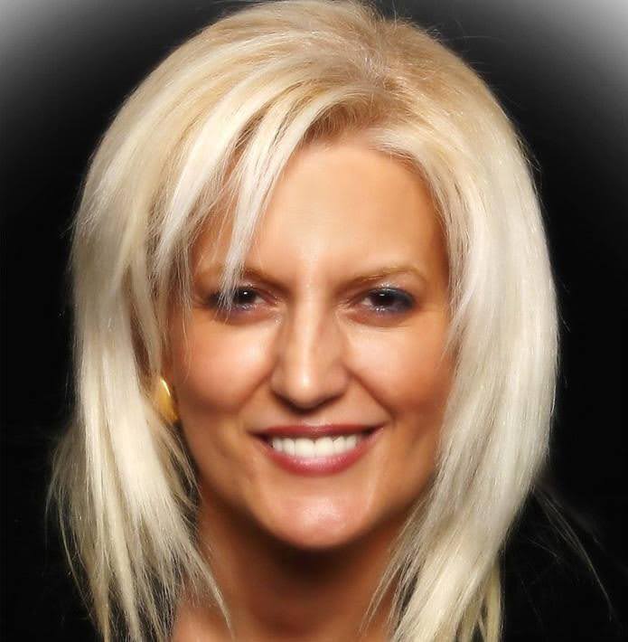 Blonde woman smiling with dark background.