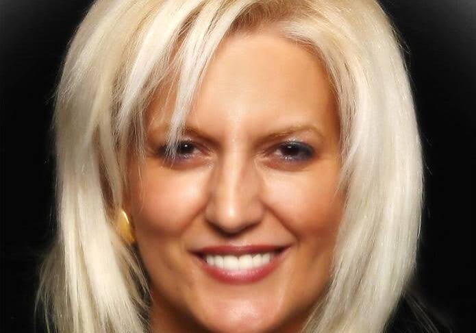 Blonde woman smiling with dark background.